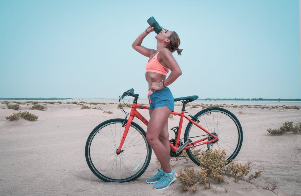 Athletic woman drinking water while biking in the Dubai desert landscape.