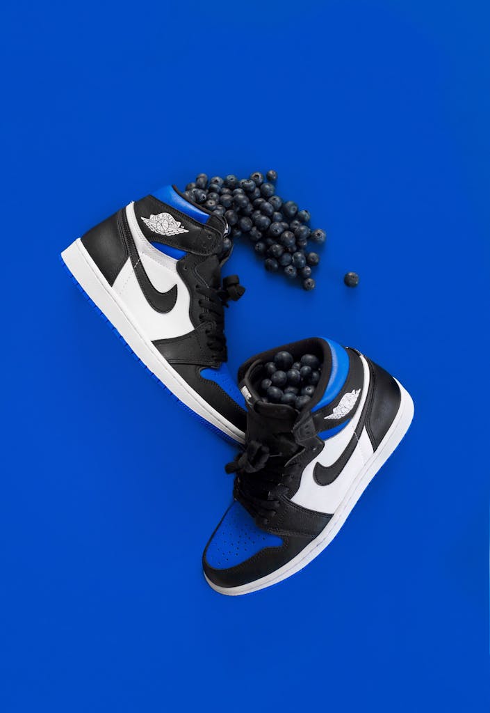 Pair of trendy black and blue sneakers surrounded by fresh blueberries on a bold blue background.